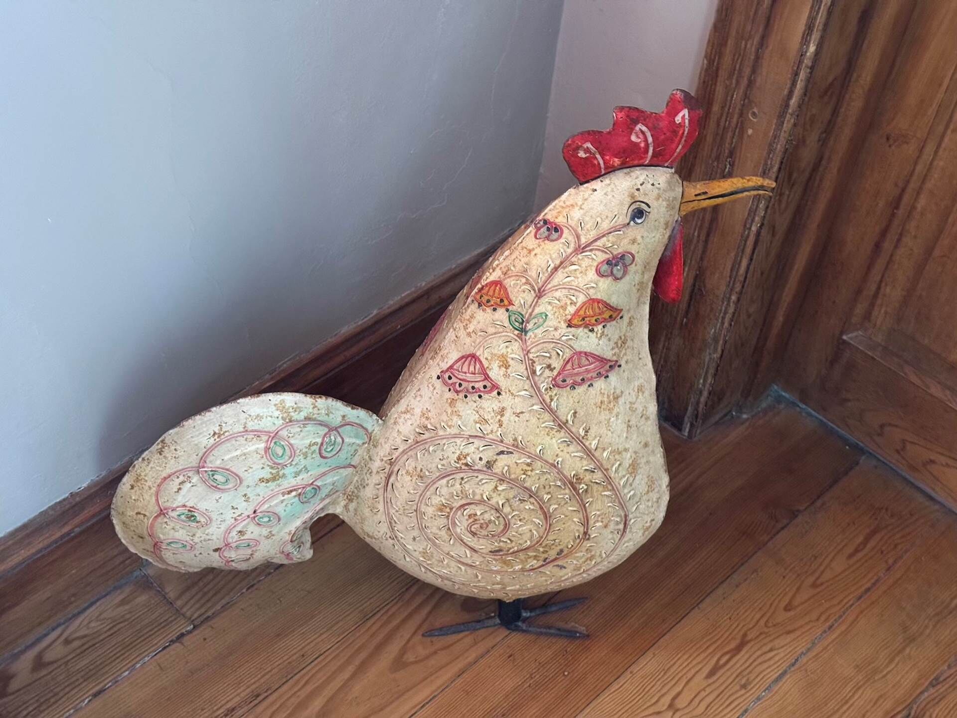 Une sculpture décorative représentant un coq, placée sur un plancher en bois près d’une porte.
