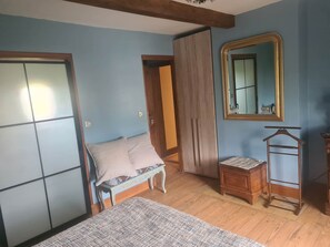 A bedroom with a bed, a wooden wardrobe, a small table, a mirror, and a hanging rack. - The Blue Room (ECHINGHEN)
