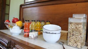 A kitchen counter with a teapot, a bowl, juice bottles, a container of granola, and a spoon.