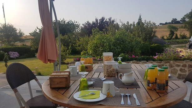 An outdoor dining area with a round wooden table set for breakfast, surrounded by wicker chairs. - La Chambre Rouge (ECHINGHEN)