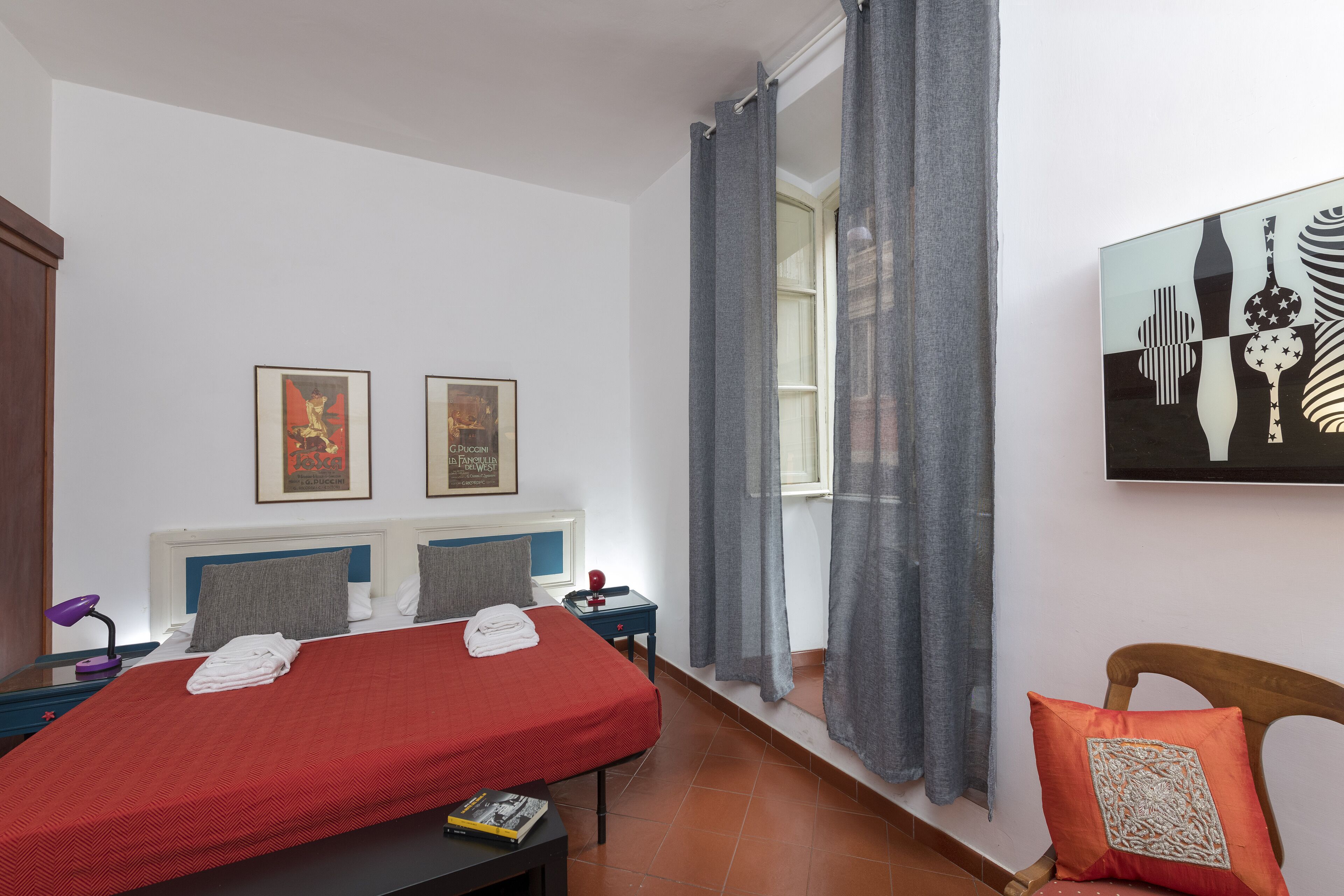 A bedroom with a bed, a nightstand, a desk, a chair, and a window with curtains.