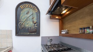 A kitchen with a gas stove, a coffee pot, and a wall-mounted sign that reads "ROYDON FISHING COMPETITION FISHING". - Opera House (Rome)