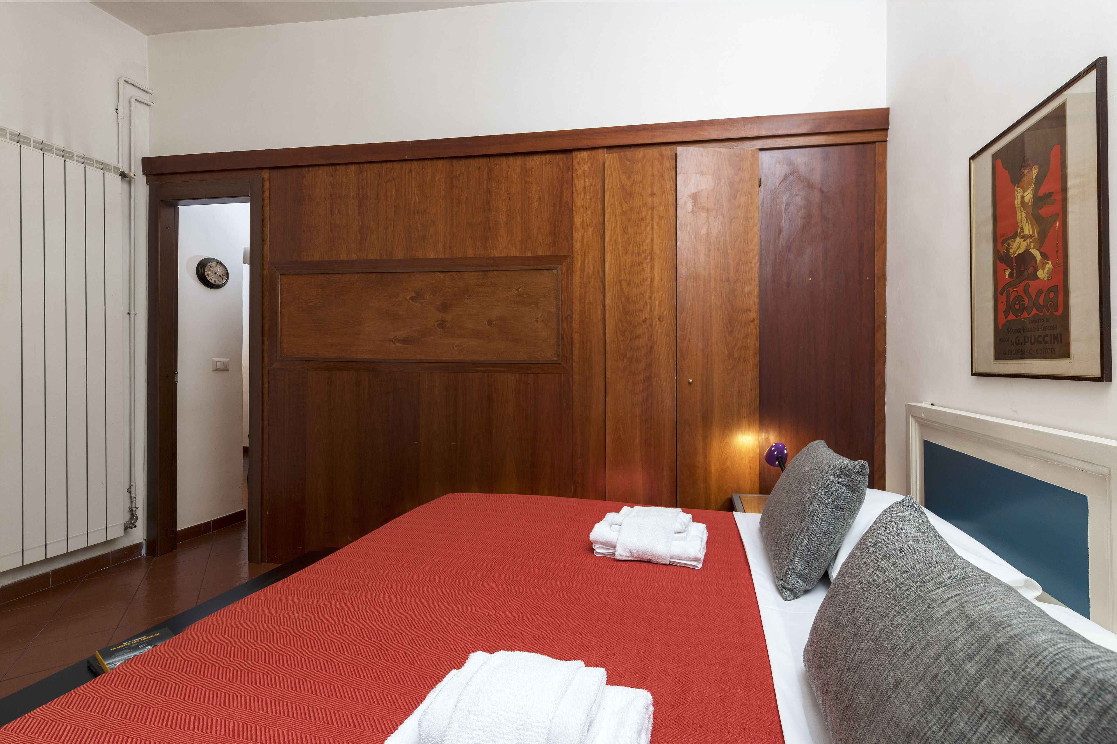 Habitación de hotel con una cama grande, paneles de madera, cubrecama rojo y un cuadro enmarcado en la pared.