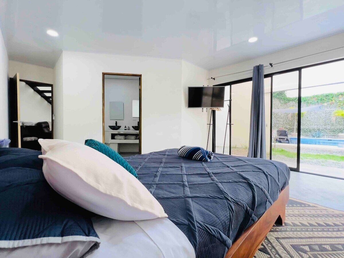 A modern bedroom with a large bed, a TV, and a view of the outdoors.