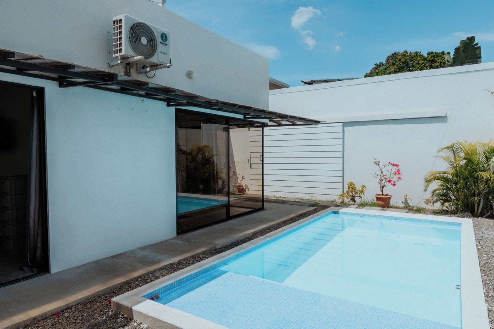 A modern house with a swimming pool, a covered patio, and a white exterior wall.