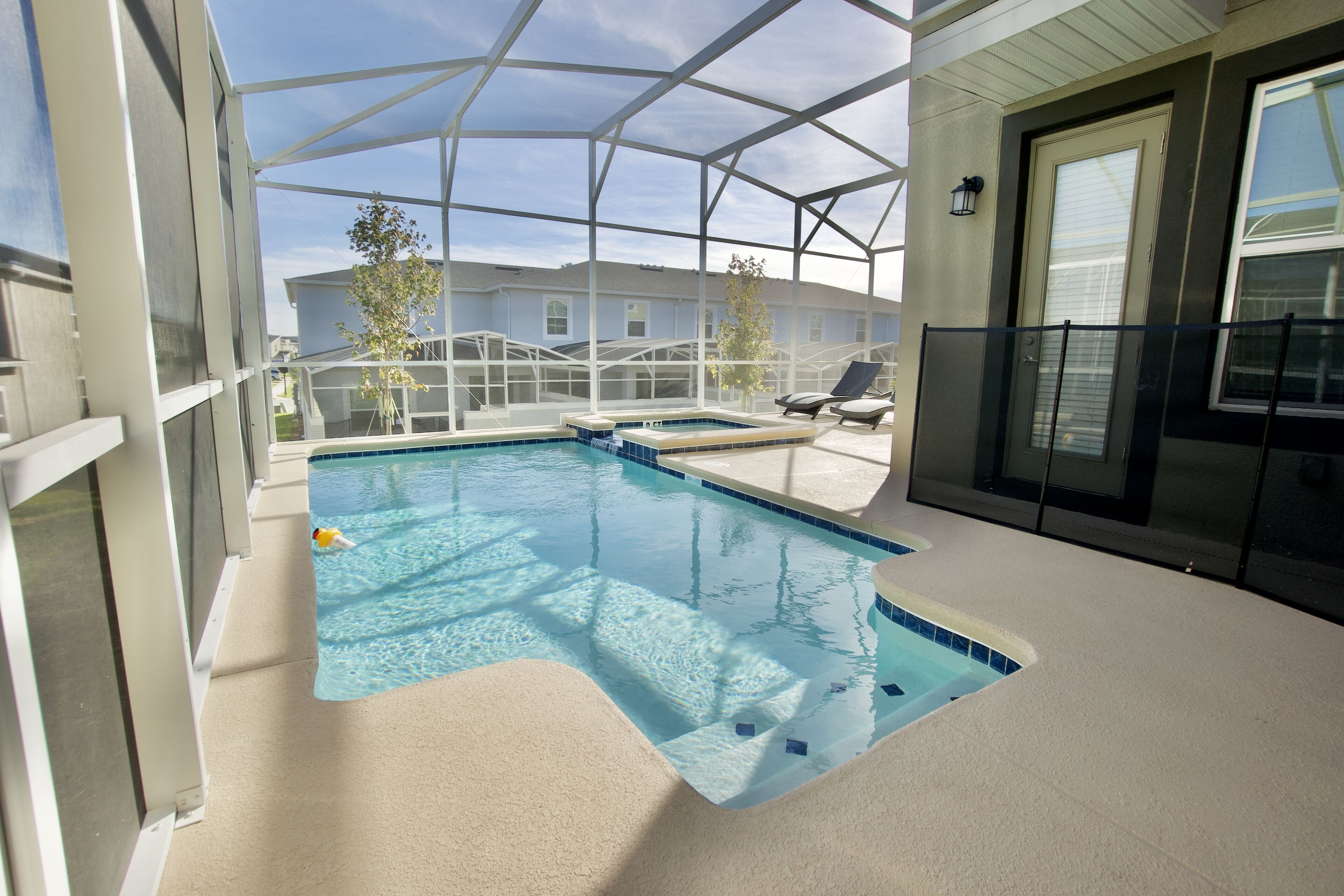 An indoor swimming pool with clear water, surrounded by a glass enclosure, and a lounge area with chairs.
