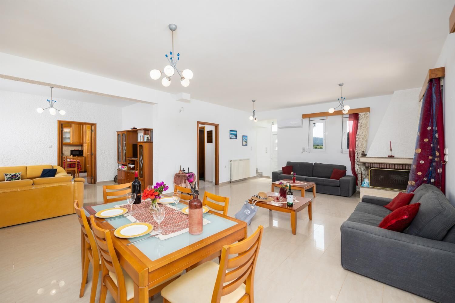 Amplia sala de estar con una mesa de comedor preparada para cuatro personas, un sofá, una chimenea y una cocina visible a través de una puerta abierta.