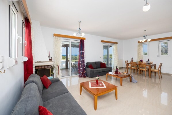 Ein geräumiges Wohnzimmer mit grauem Sofa, einem Holztisch und einem Essbereich mit Tisch und Stühlen.