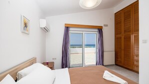 Een hotelkamer met een bed, een houten hoofdeinde, een raam met gordijnen, uitzicht op zee en een houten kledingkast.