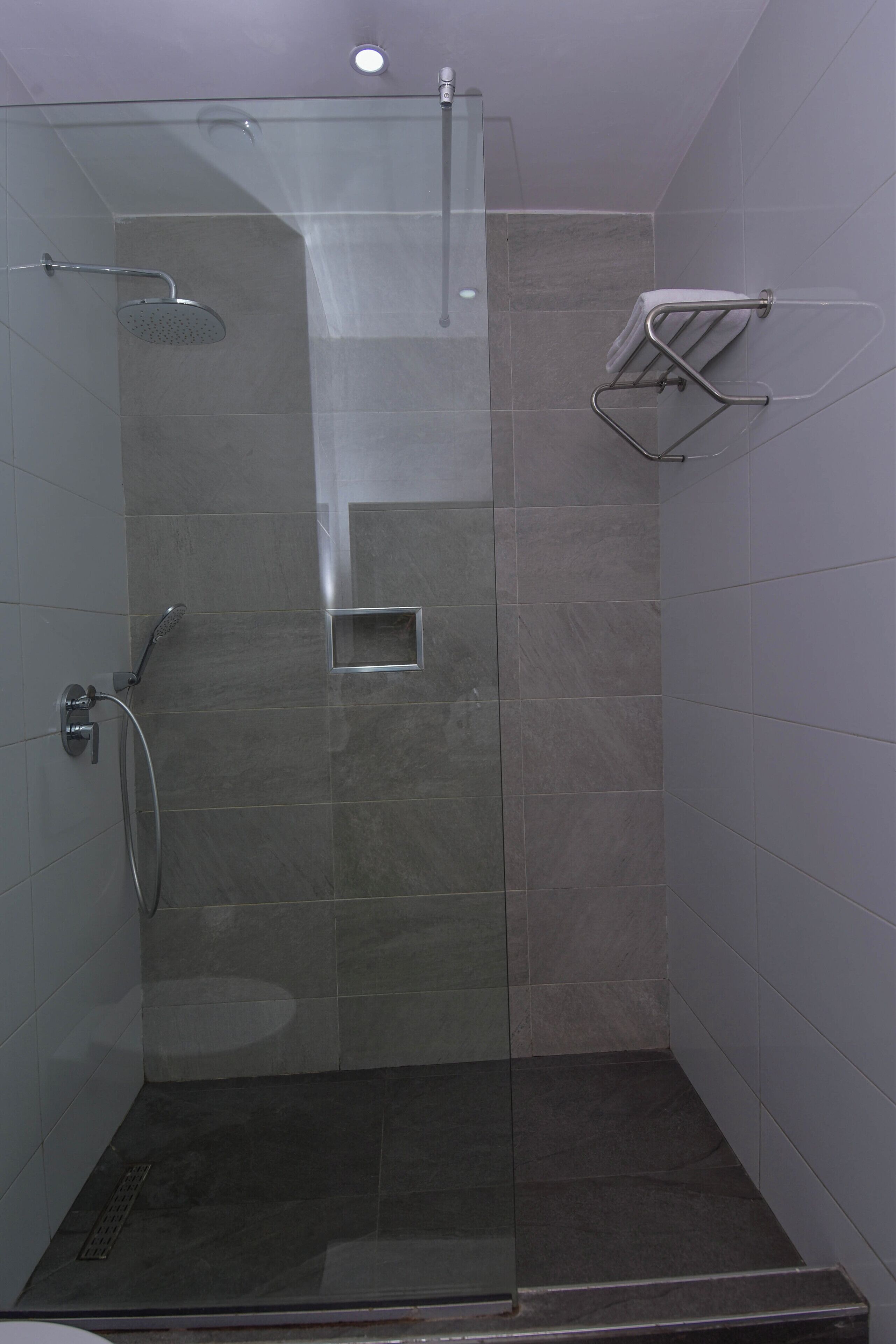 A glass-enclosed shower stall with a handheld showerhead, a towel rack, and a small square vent.