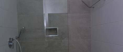 A glass-enclosed shower stall with a handheld showerhead, a towel rack, and a small square vent.
