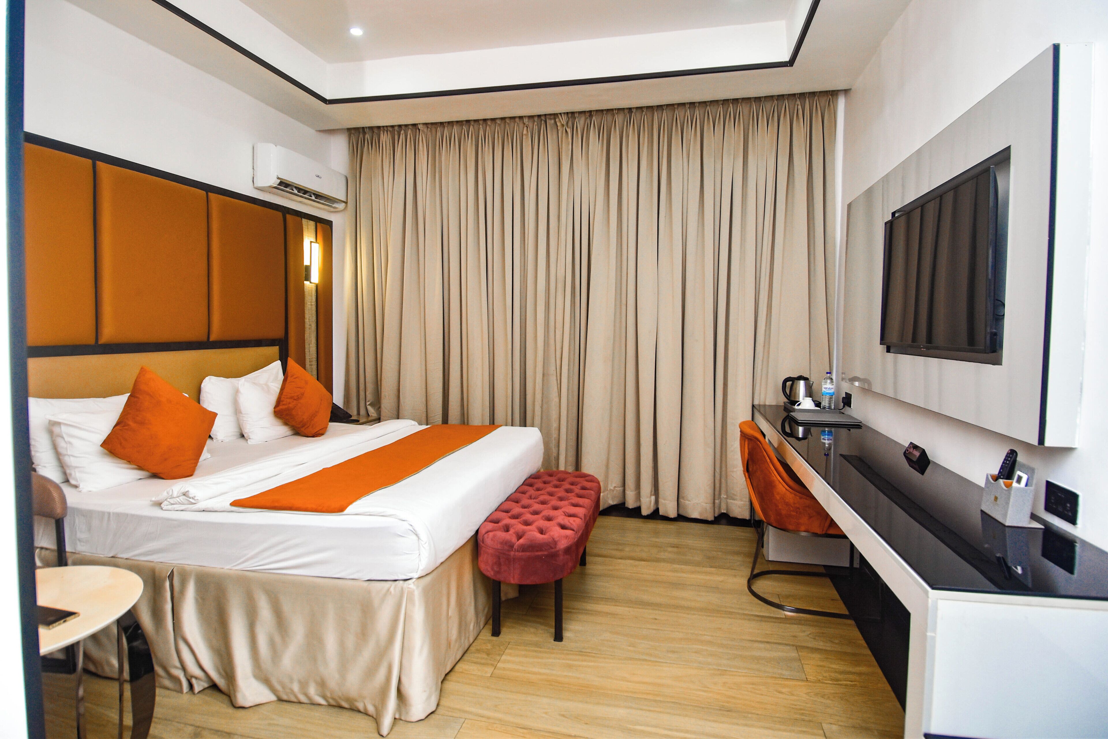 A hotel room with a bed, a desk, a chair, an air conditioning unit, and a large window with curtains.