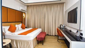 A hotel room with a bed, a desk, a chair, an air conditioning unit, and a large window with curtains.