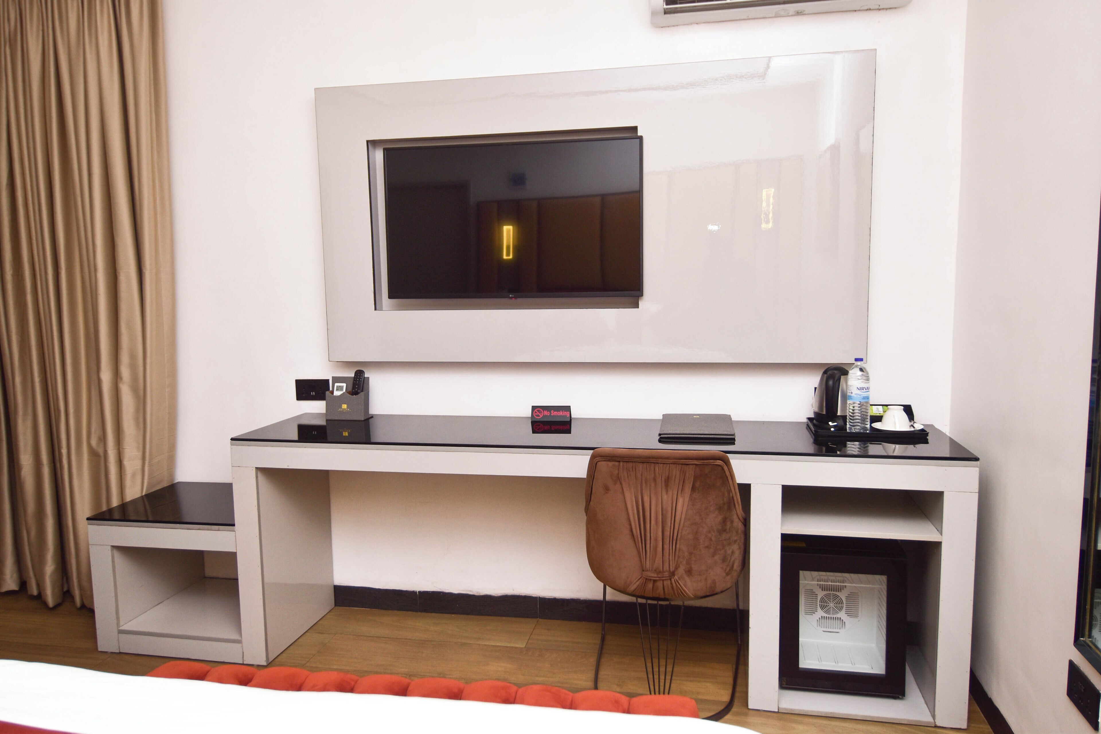 A hotel room with a desk, chair, TV, and a small cabinet.