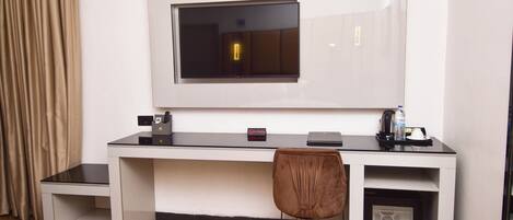 A hotel room with a desk, chair, TV, and a small cabinet.