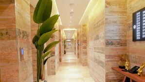 A hotel hallway with marble walls, a potted plant, and a reception desk with a telephone and decorative items. - Bayview Resorts And Hotels Lekki (Lekki)