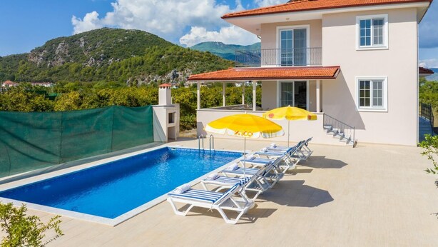 Un edificio de dos pisos con piscina, sillones de descanso y sombrillas.