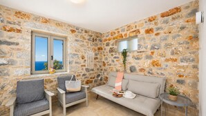 Una habitación con paredes de piedra, un sofá, dos sillones, una mesita y una ventana con vistas.