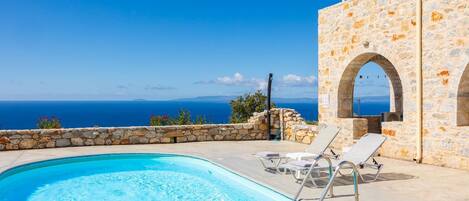 A swimming pool with clear blue water, stone walls, and a view of the sea.
