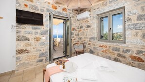 Ein Zimmer mit Steinwänden, einem Bett, einem Fernseher und einem Fenster mit Blick.
