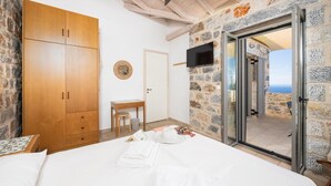 Ein Schlafzimmer mit einem großen Bett, einem Holzschrank, Steinwänden, einem kleinen Tisch mit Stuhl und einem an der Wand montierten Fernseher.