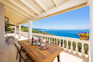 A wooden table with a bottle of wine, a book, and a decorative plate on a balcony overlooking the sea.