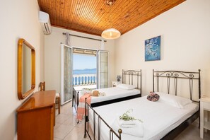 A bedroom with two beds, a wooden ceiling, a balcony with a view, and a painting on the wall.