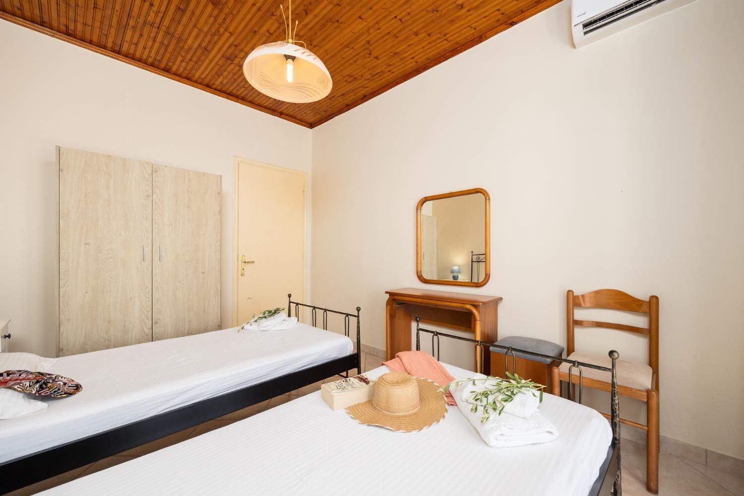 Una habitación de hotel con dos camas individuales, un armario de madera, un espejo y una silla.