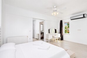 A modern bedroom with a bed, a vanity with a mirror, a ceiling fan, and an air conditioning unit.
