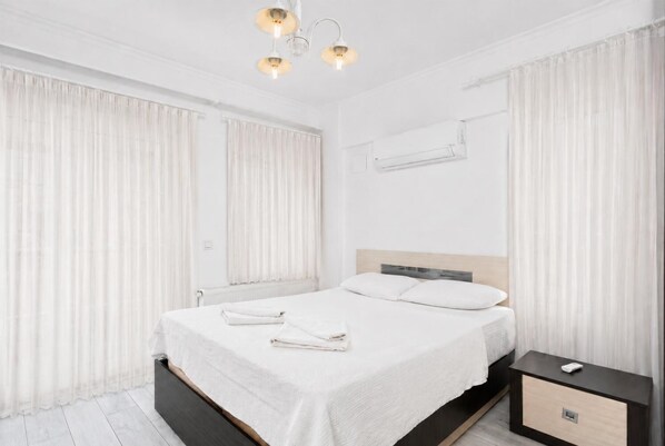 Un dormitorio moderno con una cama grande, cortinas blancas, una mesita de noche y una lámpara en el techo.