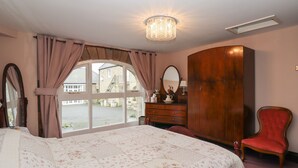 Een slaapkamer met een groot bed, een houten garderobe, een rode stoel en een raam met gordijnen.