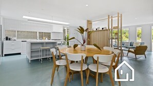 A modern kitchen with white cabinetry, a wooden dining table with chairs, and a large window. - Villa Santorini *1 NIGHT FREE* Secluded Back Beach Poolside Oasis (Blairgowrie)