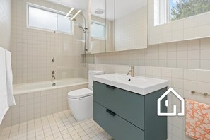 A modern bathroom with a bathtub, toilet, sink, and a large mirror. - Villa Santorini *1 NIGHT FREE* Secluded Back Beach Poolside Oasis (Blairgowrie)