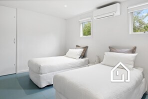 A bedroom with two beds, white bedding, a window, and an air conditioning unit. - Villa Santorini *1 NIGHT FREE* Secluded Back Beach Poolside Oasis (Blairgowrie)