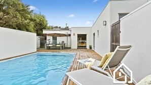 A modern outdoor pool area with a wooden deck, lounge chairs, and a dining area with a table and chairs. - Villa Santorini *1 NIGHT FREE* Secluded Back Beach Poolside Oasis (Blairgowrie)