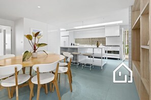 A modern kitchen with white cabinets, a central island with bar stools, and a dining area with a round table and chairs. - Villa Santorini *1 NIGHT FREE* Secluded Back Beach Poolside Oasis (Blairgowrie)