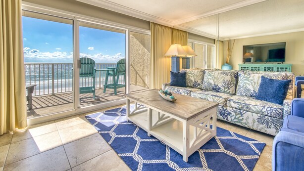 A living room with a sofa, coffee table, and a TV. There is a balcony with a view of the ocean. - B404 | Beachfront with Beach Service, Pool, & WiFi (Miramar Beach)