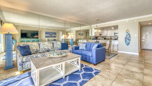 A spacious living room with two sofas, a coffee table, and a kitchen in the background. - B404 | Beachfront with Beach Service, Pool, & WiFi (Miramar Beach)