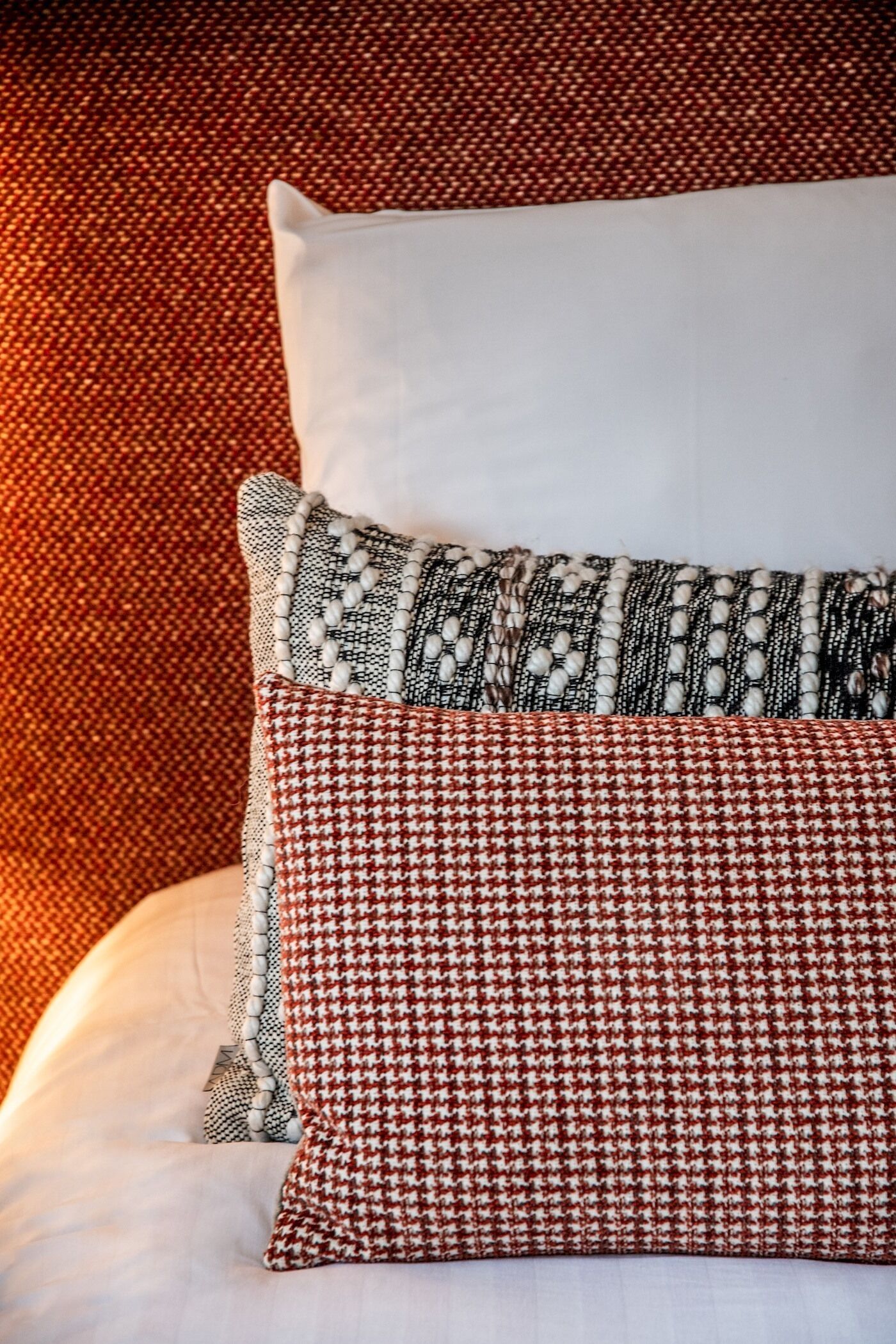 Un lit avec une literie blanche et deux coussins décoratifs, l’un à motif pied-de-poule et l’autre à rayures.