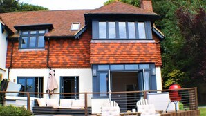 Ein zweistöckiges Haus mit Ziegelaußenwand, großen Fenstern und einer Terrasse mit Gartenmöbeln.