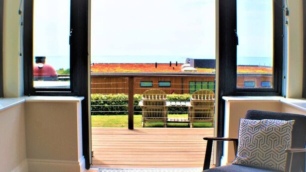 Ein Zimmer mit Meerblick durch große Fenster, einer Holzterrasse und Sitzgelegenheiten im Freien.