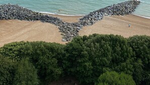 Ein Strand mit einem steinernen Wellenbrecher, blauem Himmel und ruhiger See.