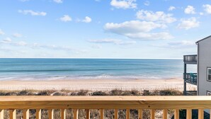 Vista a la playa desde un balcón con barandilla de madera, con vista a una playa de arena y el océano.