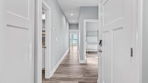 Un pasillo con puertas blancas, suelo de madera y vista a un balcón.