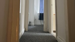 Ein schmaler Korridor mit Teppichboden, der zu einem Zimmer mit Fenster und blauem Vorhang führt.