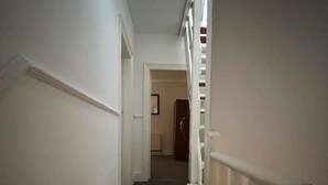 Ein schmaler, mit Teppich belegter Gang mit weißen Wänden und einer Treppe auf der rechten Seite.