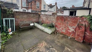 Ein Garten mit Ziegelmauer, grünem Tor und Betonboden.