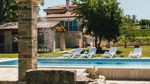 Un espace piscine avec des chaises longues, un pilier en pierre et un bâtiment doté d’un toit en tuiles.