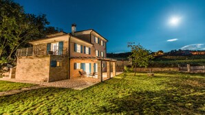 Une maison à deux étages avec une façade en pierre, un balcon et une terrasse aménagée avec du mobilier d’extérieur.