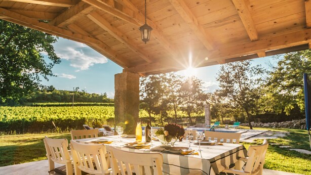 Un espace de restauration en plein air agrémenté d’une pergola en bois, d’une table dressée pour quatre personnes et de chaises avec des coussins.